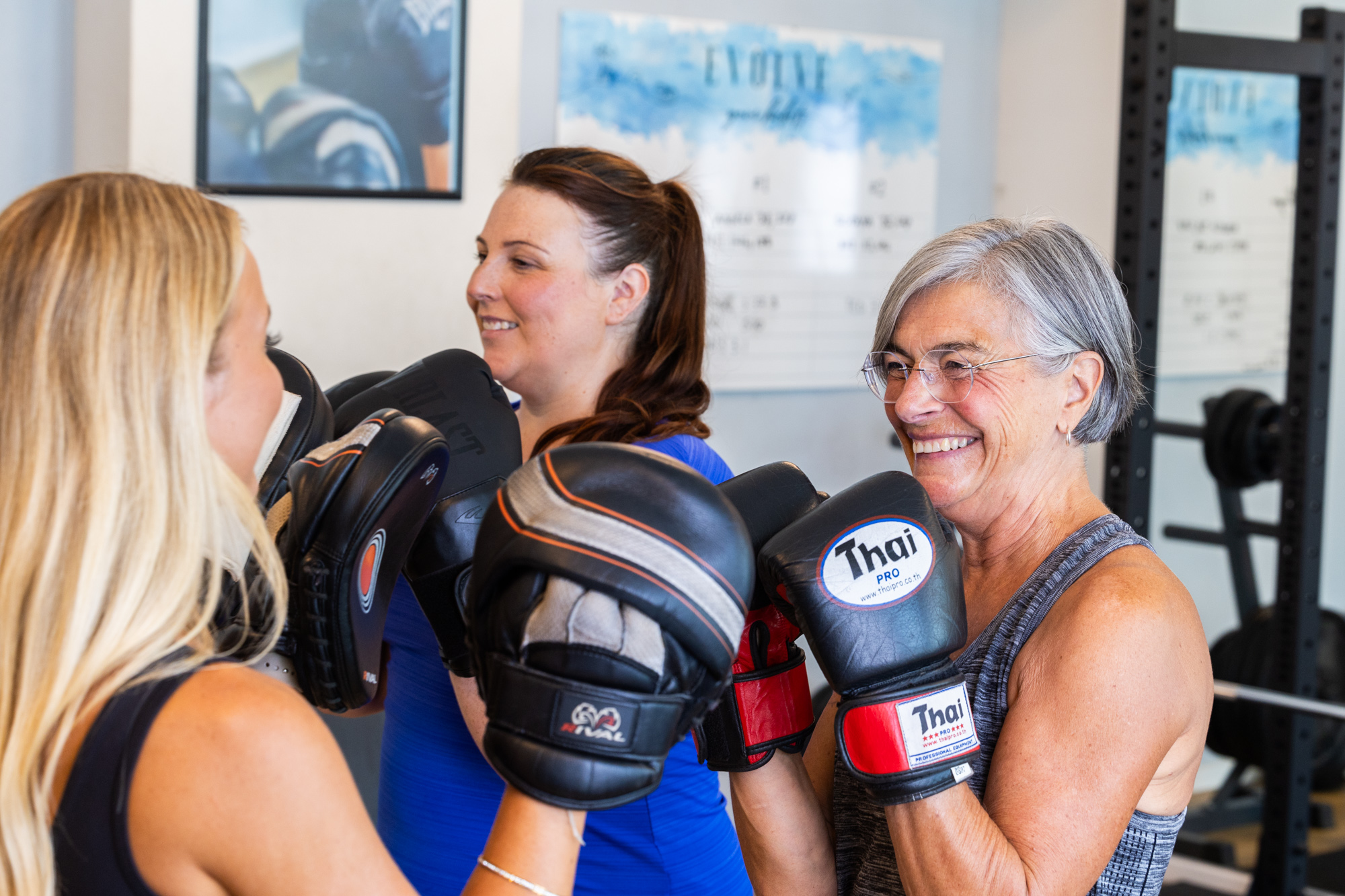 Kaz, an Evolve member, smiling mid-session with her coach during a boxing pad round